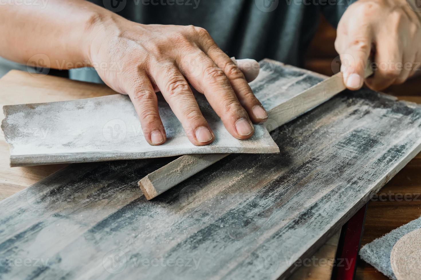 carpinteiro usa papel abrasivo de lixamento seco para polir madeira na oficina, fabricante de bricolage e conceito de marcenaria. foco seletivo foto