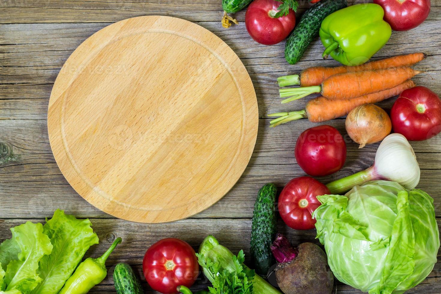 tábua de cortar círculo e legumes em fundo de madeira. Alimentação saudável foto