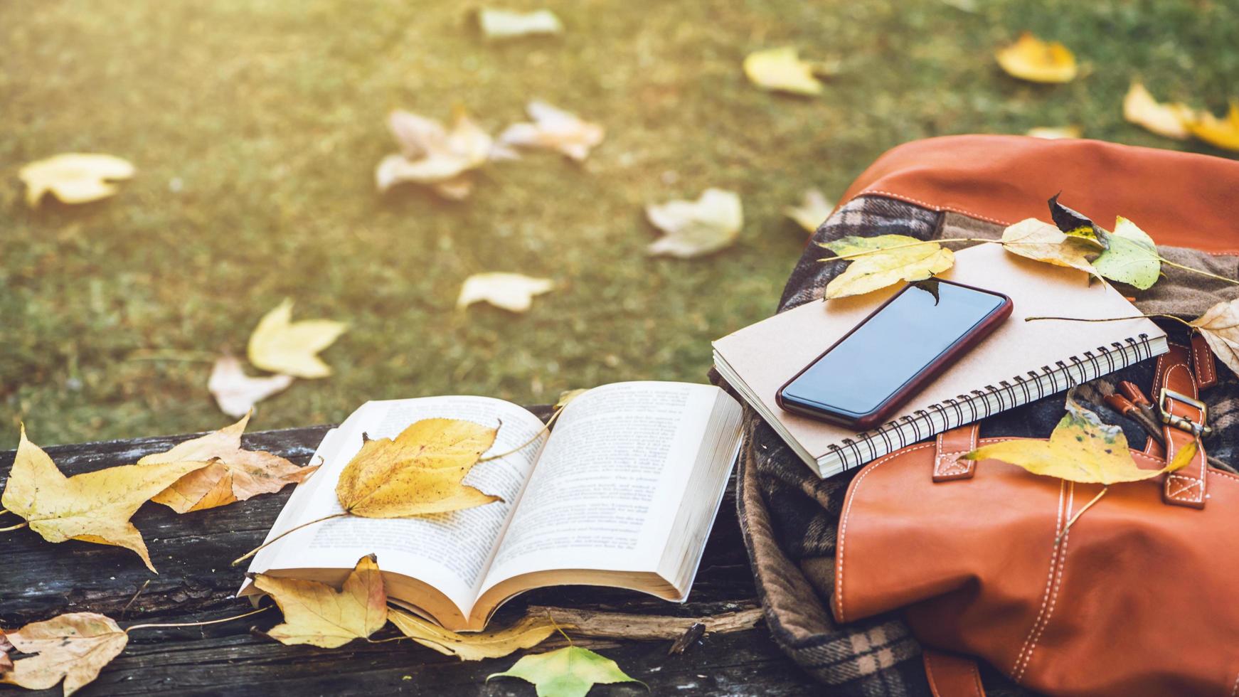 a mochila é colocada em uma mesa de madeira antiga com livros, cadernos, telefones e a natureza das folhas de bordo da vista superior. foto