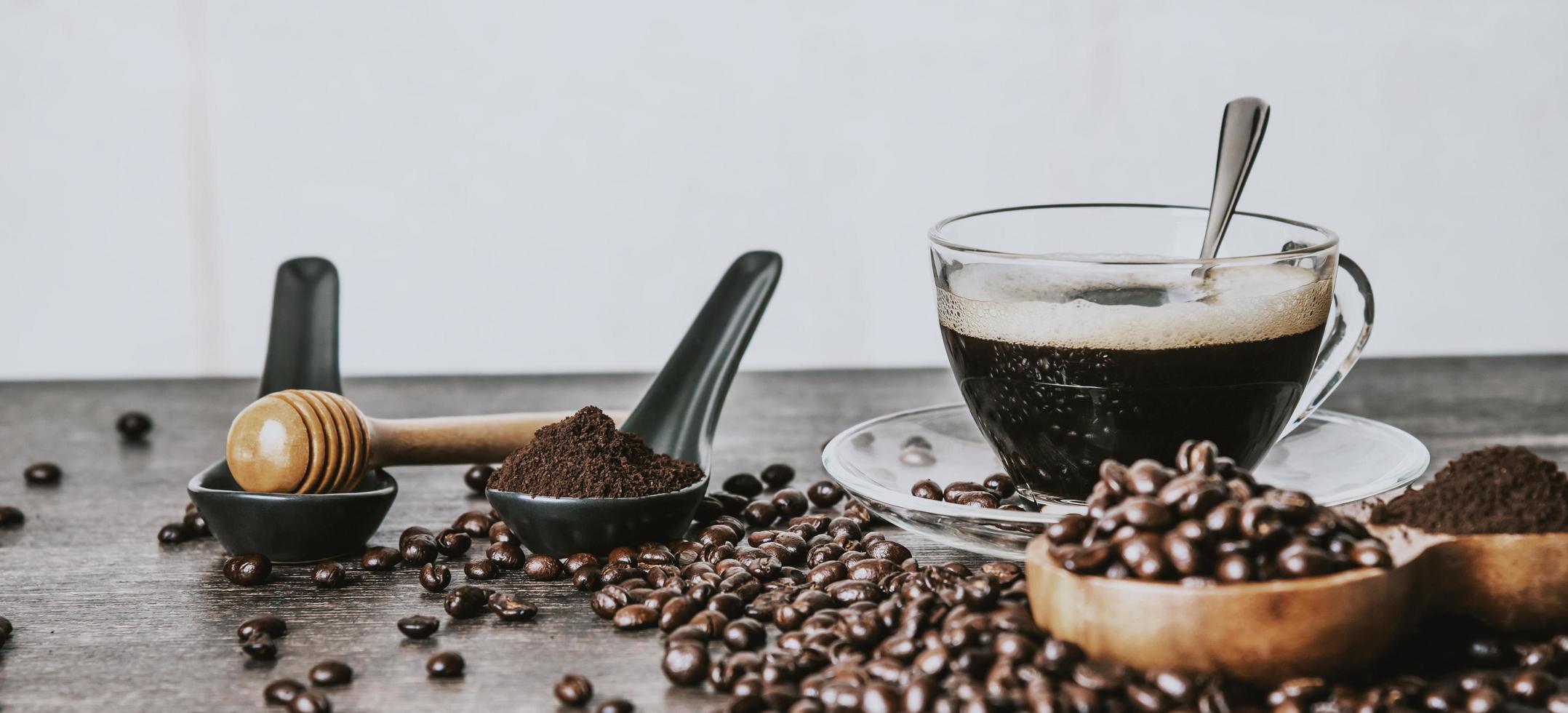 xícara de café e grãos de café torrados no saco e mel em um fundo de mesa de madeira foto