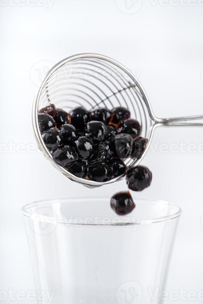 fazendo chá de bolhas, colher e despeje bolas de bolha de pérola de tapioca sabor açúcar mascavo cozido no copo no fundo da mesa de madeira branca, close-up, copie o espaço. foto