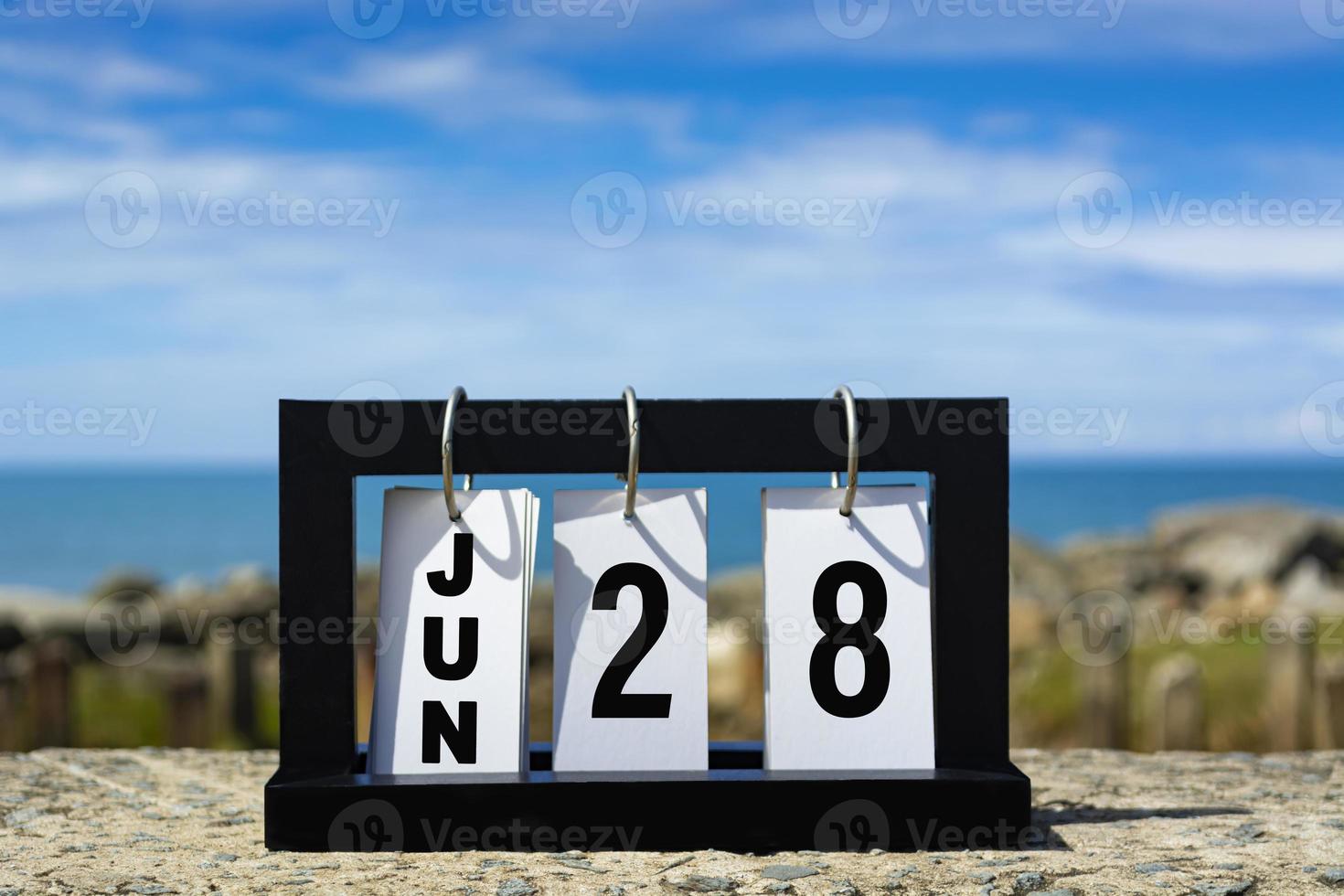 texto de data de calendário de 28 de junho na moldura de madeira com fundo desfocado do oceano. foto