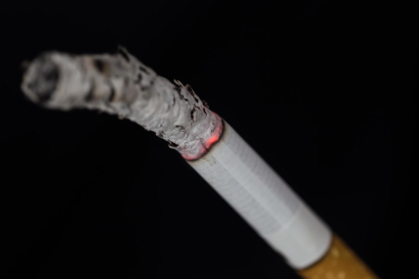 cigarro aceso com fumaça em fundo preto foto