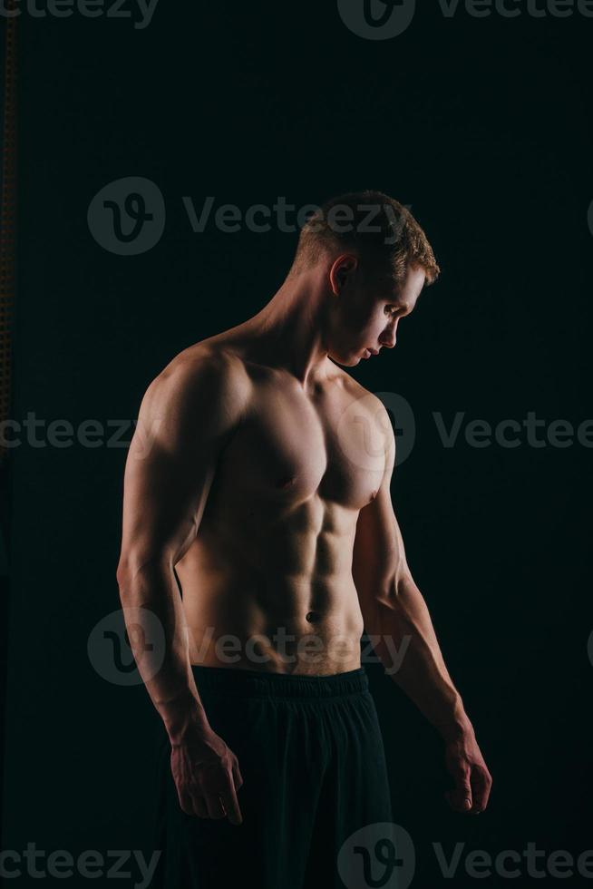 homem jovem musculoso mostrando seus bíceps isolados no fundo preto foto