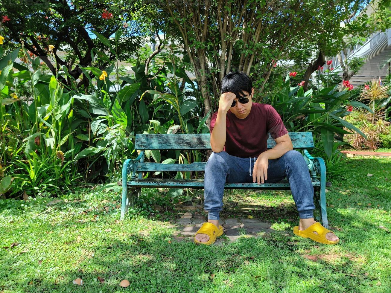 jovem asiático com cabelo preto está sentado em um banco. estresse e ansiedade. o que você está pensando na cidade do parque de verão foto