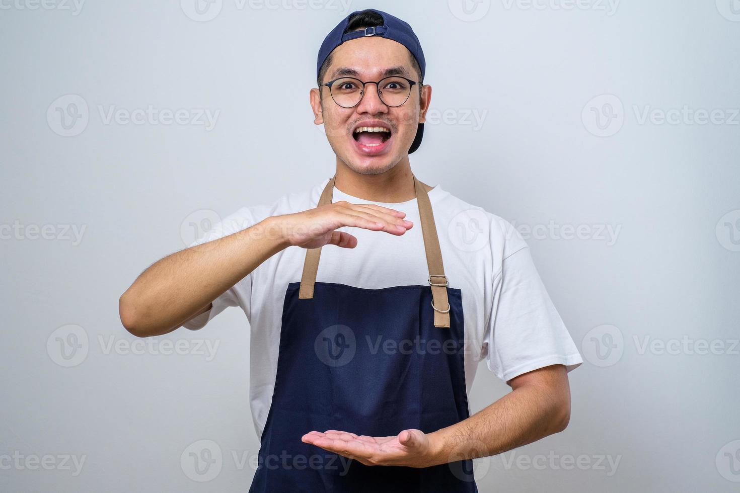 homem asiático barista gesticulando com as mãos mostrando sinal de tamanho grande e grande, símbolo de medida. sorrindo olhando para a câmera. conceito de medição. foto