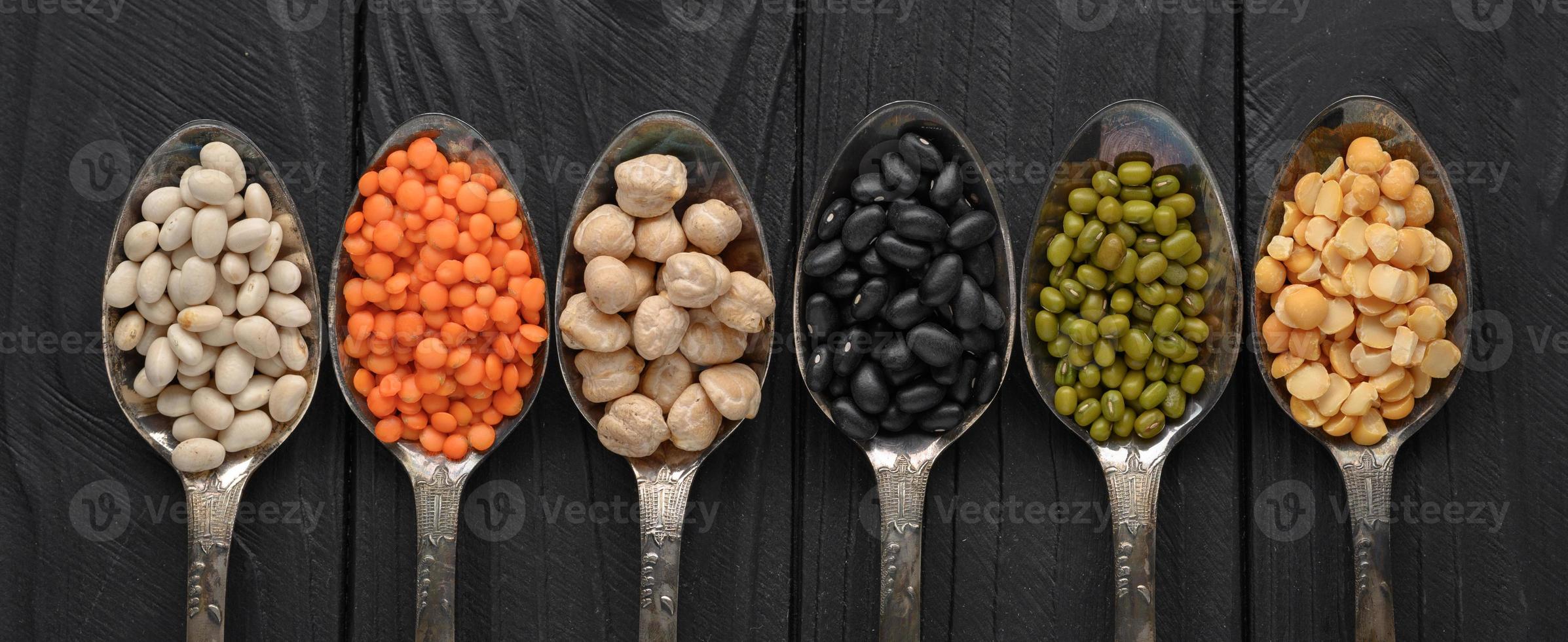 variedade de legumes em colheres de prata velhas em um fundo preto de madeira. foto
