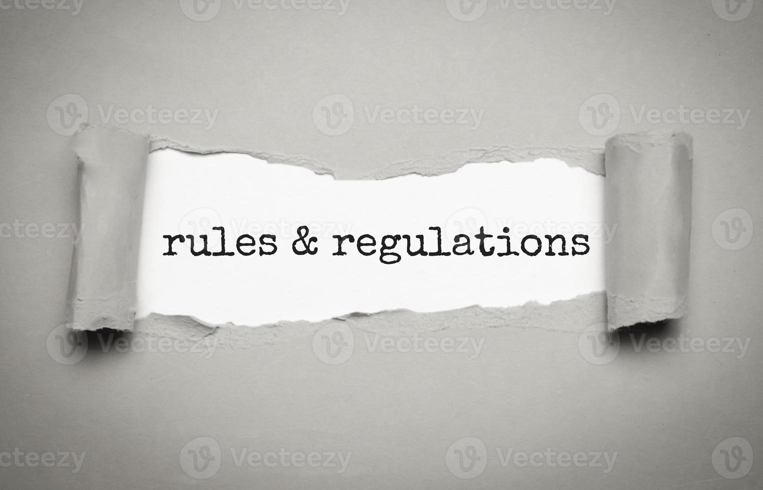 palavra de regras e regulamentos sob papel cinza rasgado foto