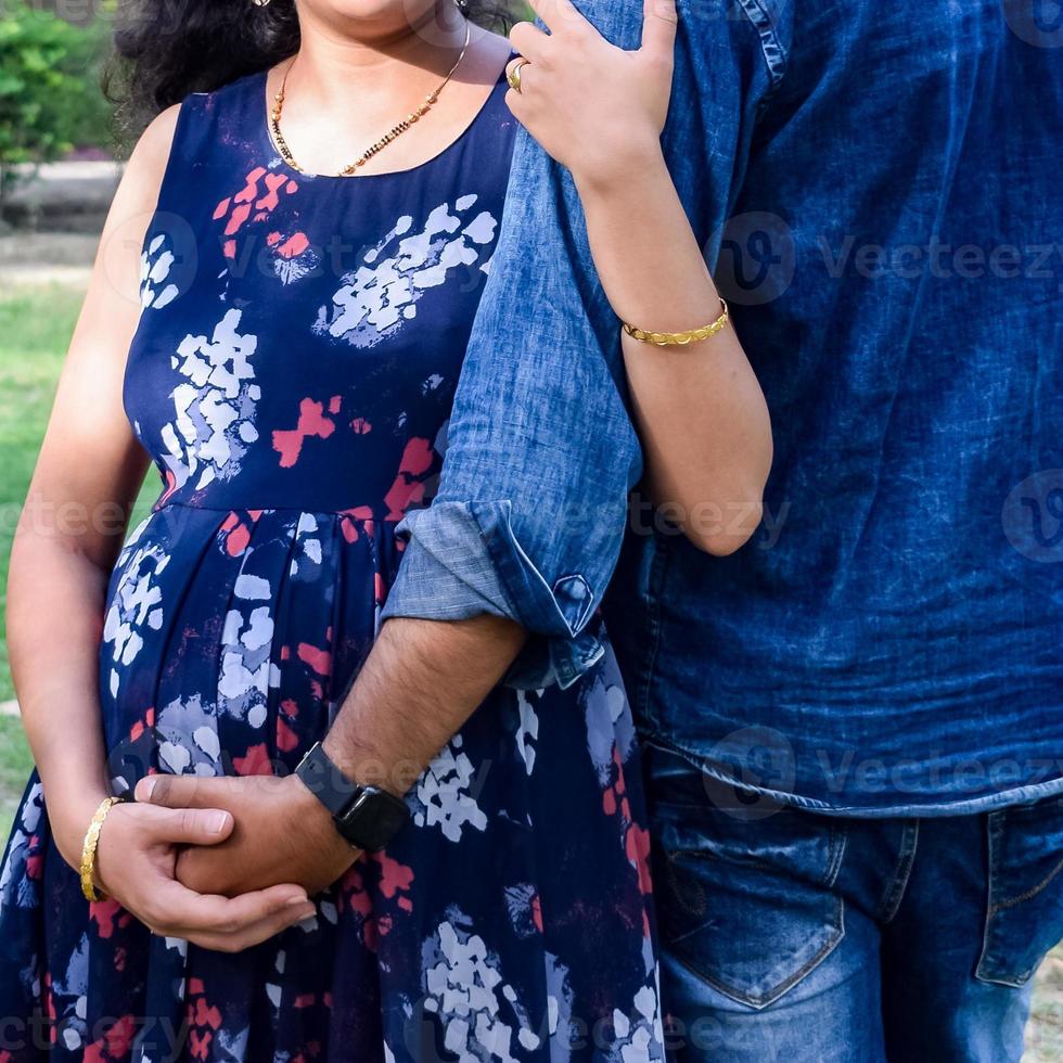 casal indiano posando para ensaio de maternidade. o casal está posando em um gramado com grama verde e a mulher está vacilando sua barriga no jardim lodhi em nova delhi, índia foto