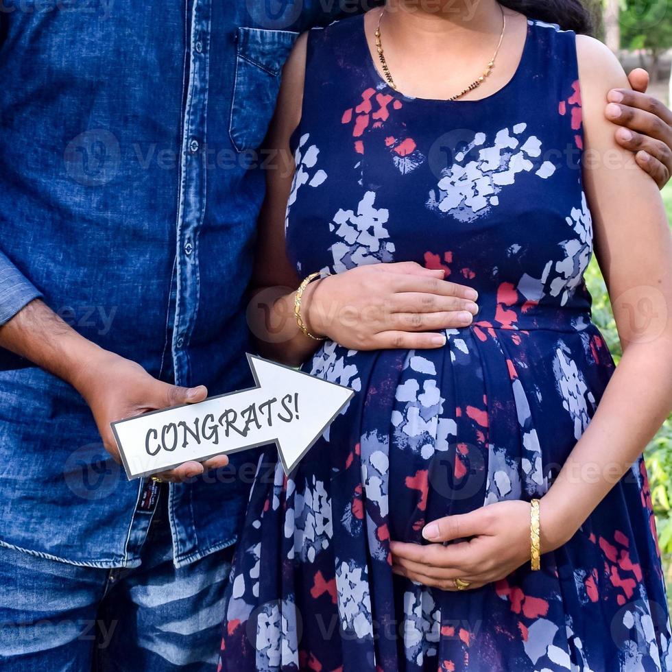 casal indiano posando para ensaio de maternidade. o casal está posando em um gramado com grama verde e a mulher está vacilando sua barriga no jardim lodhi em nova delhi, índia foto