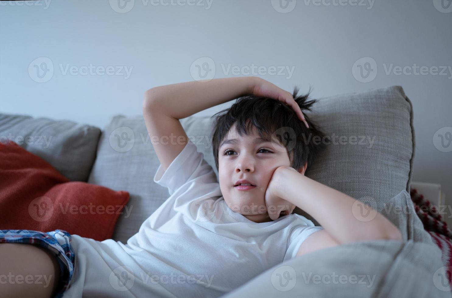 retrato menino com cara de curioso sentado no sofá assistindo desenho animado, garoto da escola sentado sozinho no sofá relaxando na sala de estar depois de voltar da escola. foto