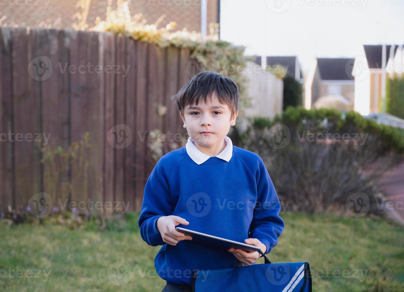 menino criança feliz segurando o tablet pc do lado de fora esperando o ônibus escolar, garoto retrato jogando jogo online ou lendo strory na internet, menino pré-escolar aprendendo com tecnologia moderna foto