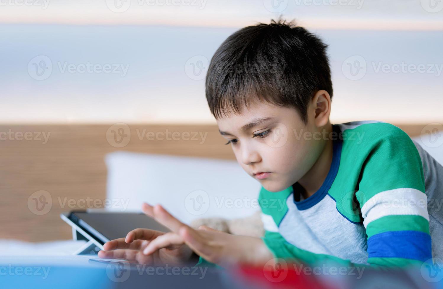 criança jogando jogos online na internet no quarto, retrato de menino  usando tablet digitando ou conversando com amigos de manhã, infância  sentada na cama fazendo lição de casa, criança da escola com