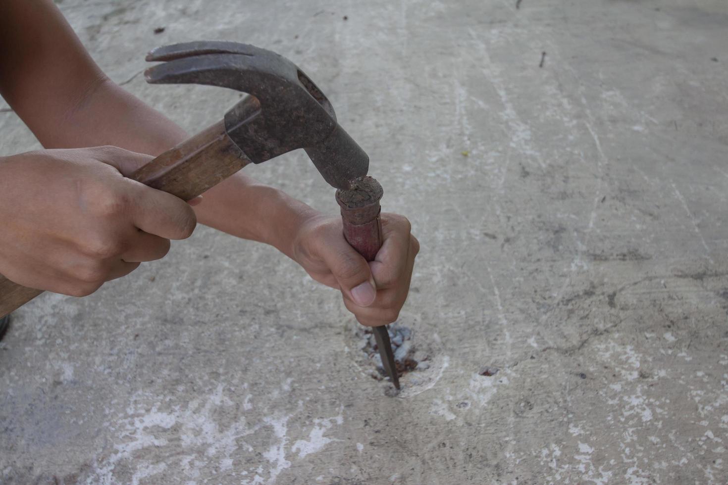 mão segurando o martelo e o cinzel para extrair o piso de cimento. foto