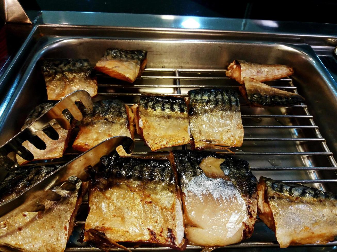 fatia de saba grelhado e frito na bandeja de grelha de aço de comida com pinças. comida saudável e peixe fresco cortado foto