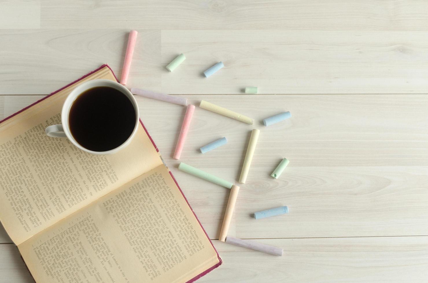 uma xícara de café, um livro aberto e giz multicolorido sobre um fundo branco de madeira. de volta à escola, dia mundial do livro. foto