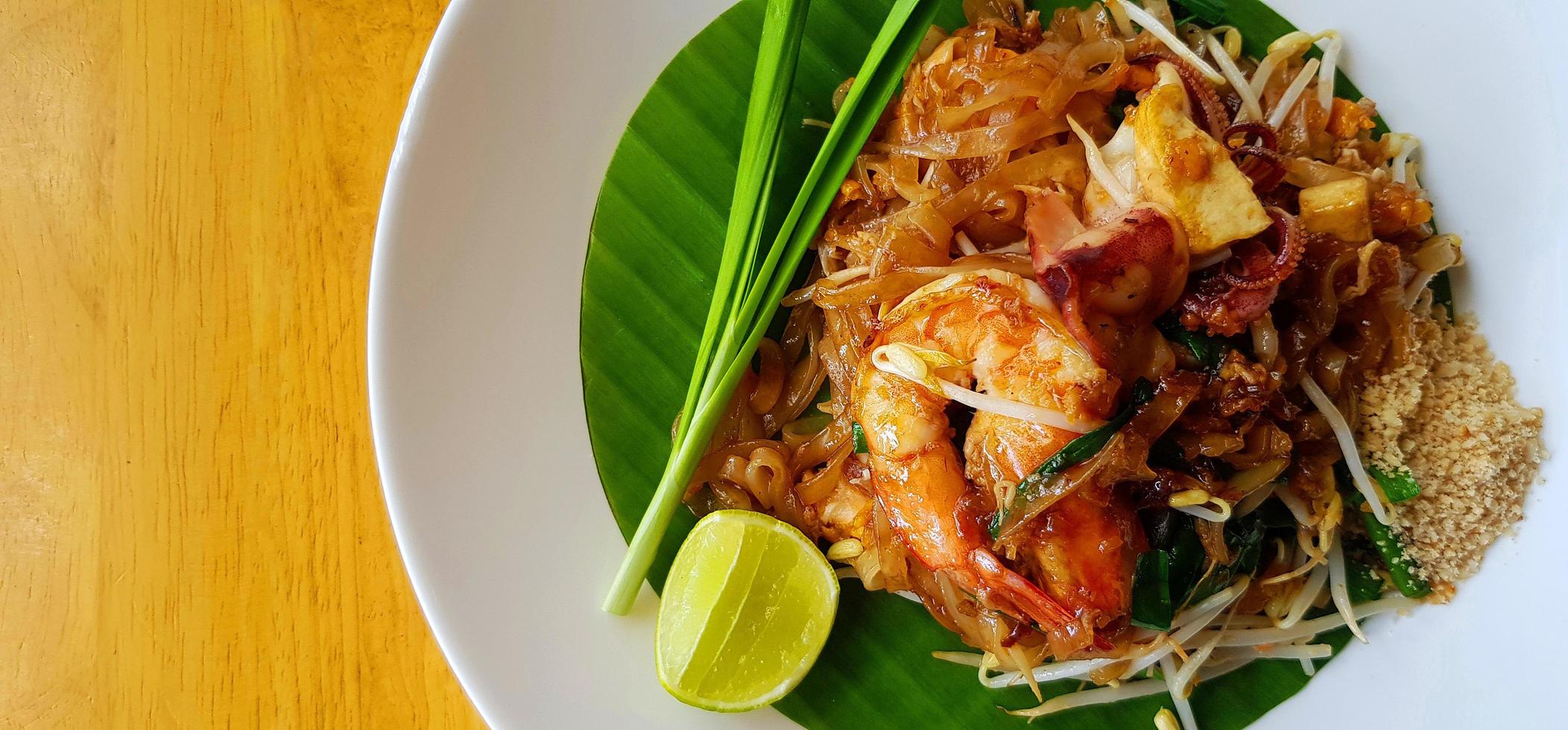 vista superior do refogado com macarrão de arroz, camarão do rio ou camarão, broto de feijão, cebolinha fatiada e limão na folha de bananeira com espaço de cópia. comida famosa na tailândia call pad thai. técnica de foco seletivo. foto