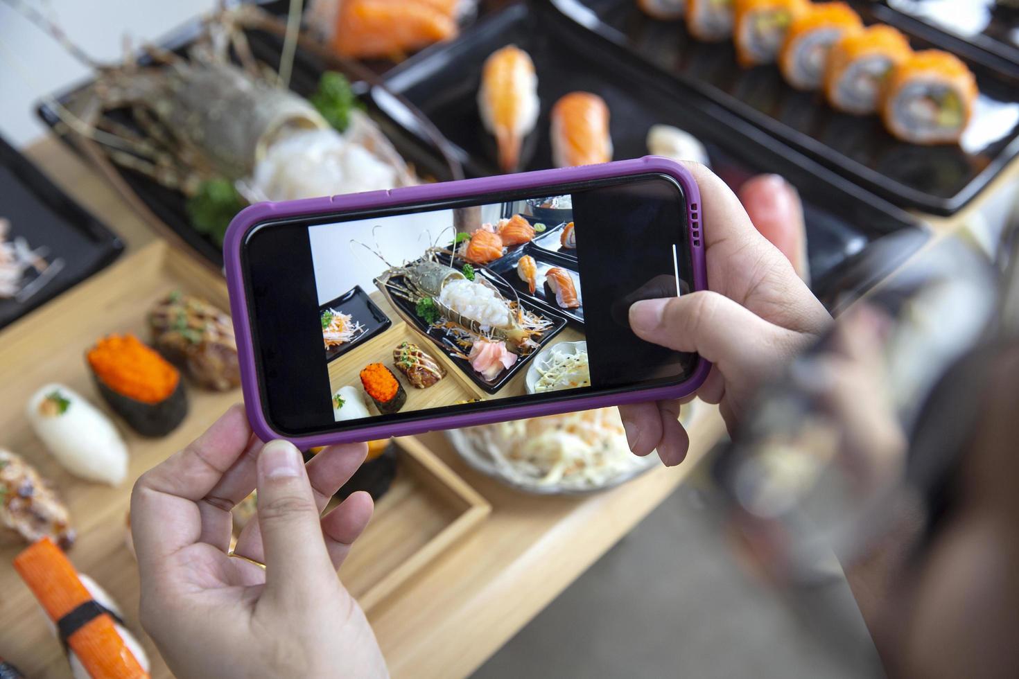 mulher fotografando comida servida conjunto de sushi japonês, rolos de sushi nigiri e sashimi no menu do restaurante de comida japonesa foto