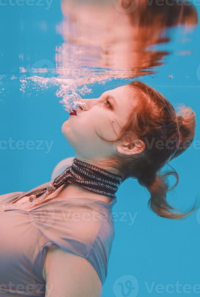 retrato de arte surreal de jovem de vestido cinza e cachecol frisado debaixo d'água na piscina foto