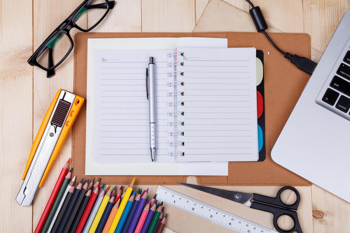 local de trabalho com lápis de cor e suprimentos, laptop, notebook, óculos na mesa de madeira foto
