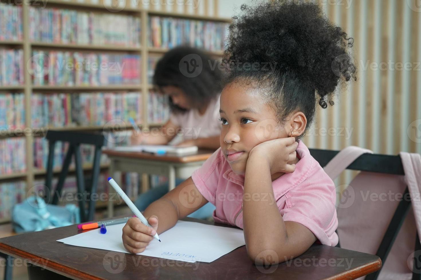 criança pré-escolar desenhando com lápis de cor em papel branco na mesa em sala de aula com amigos foto