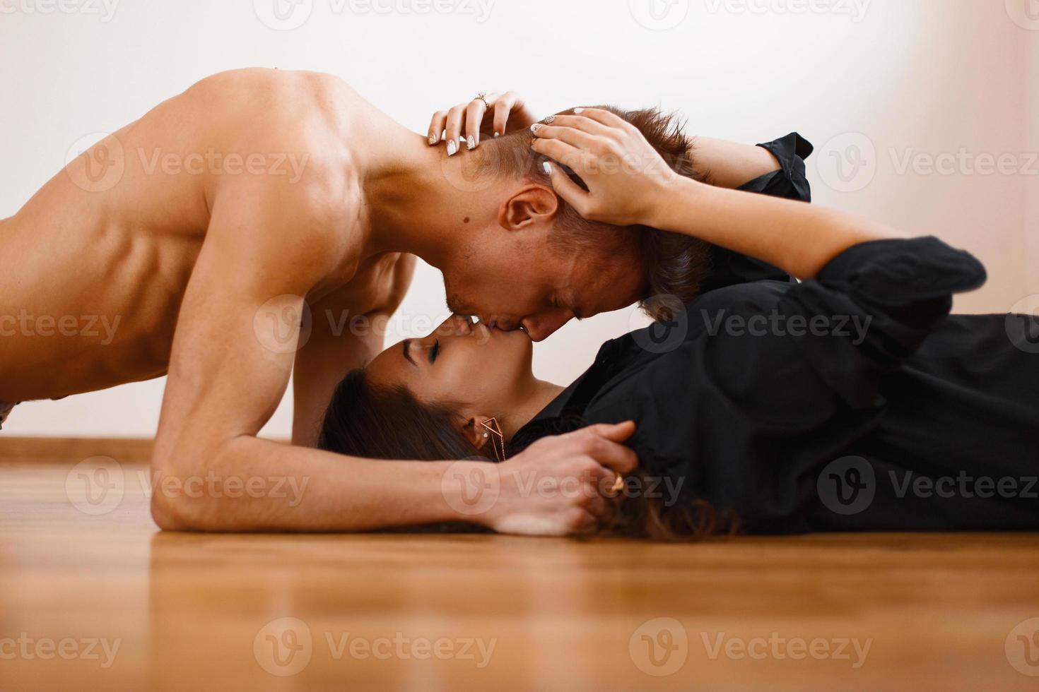 jovem casal lindo beijando no chão de madeira. homem bonito deitado sobre a garota e beijando foto