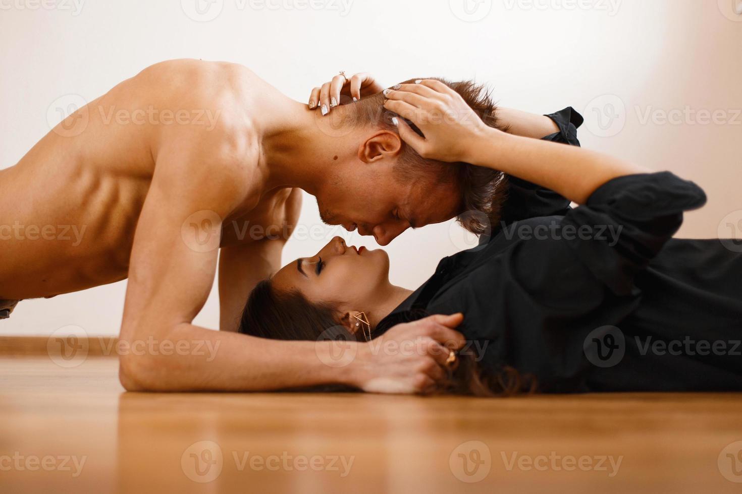 jovem casal lindo deitado no chão de madeira. homem bonito deitado sobre a garota e olha para ela foto