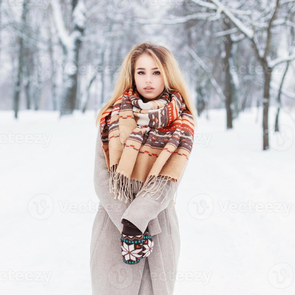 linda garota com um casaco de inverno e cachecol fica no parque foto