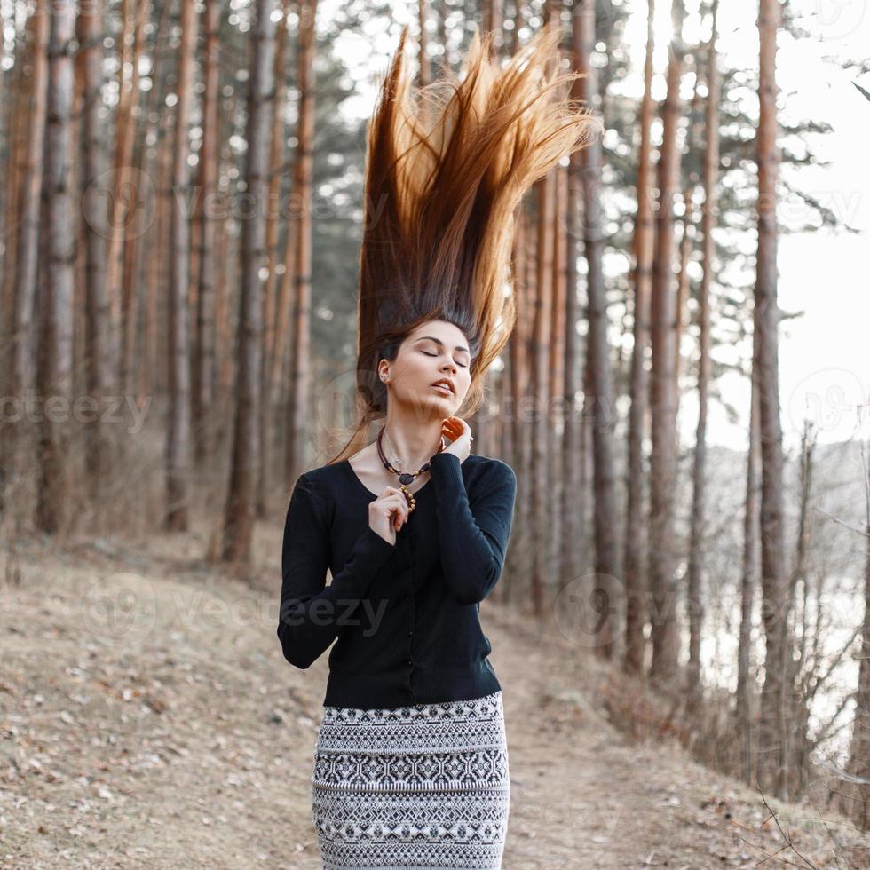 linda jovem em um vestido preto em pé no parque. cabelo voando para cima. foto