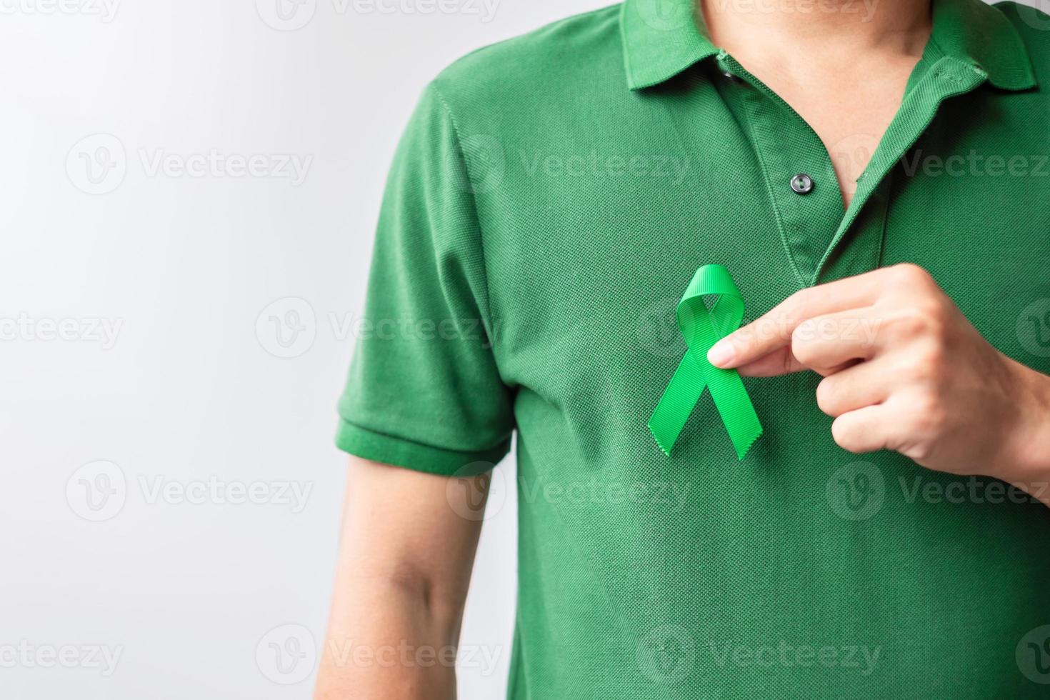 mão segurando a fita verde para fígado, vesícula biliar, ducto biliar, cervical, câncer renal e mês de conscientização do linfoma. conceito de saúde e dia mundial do câncer foto