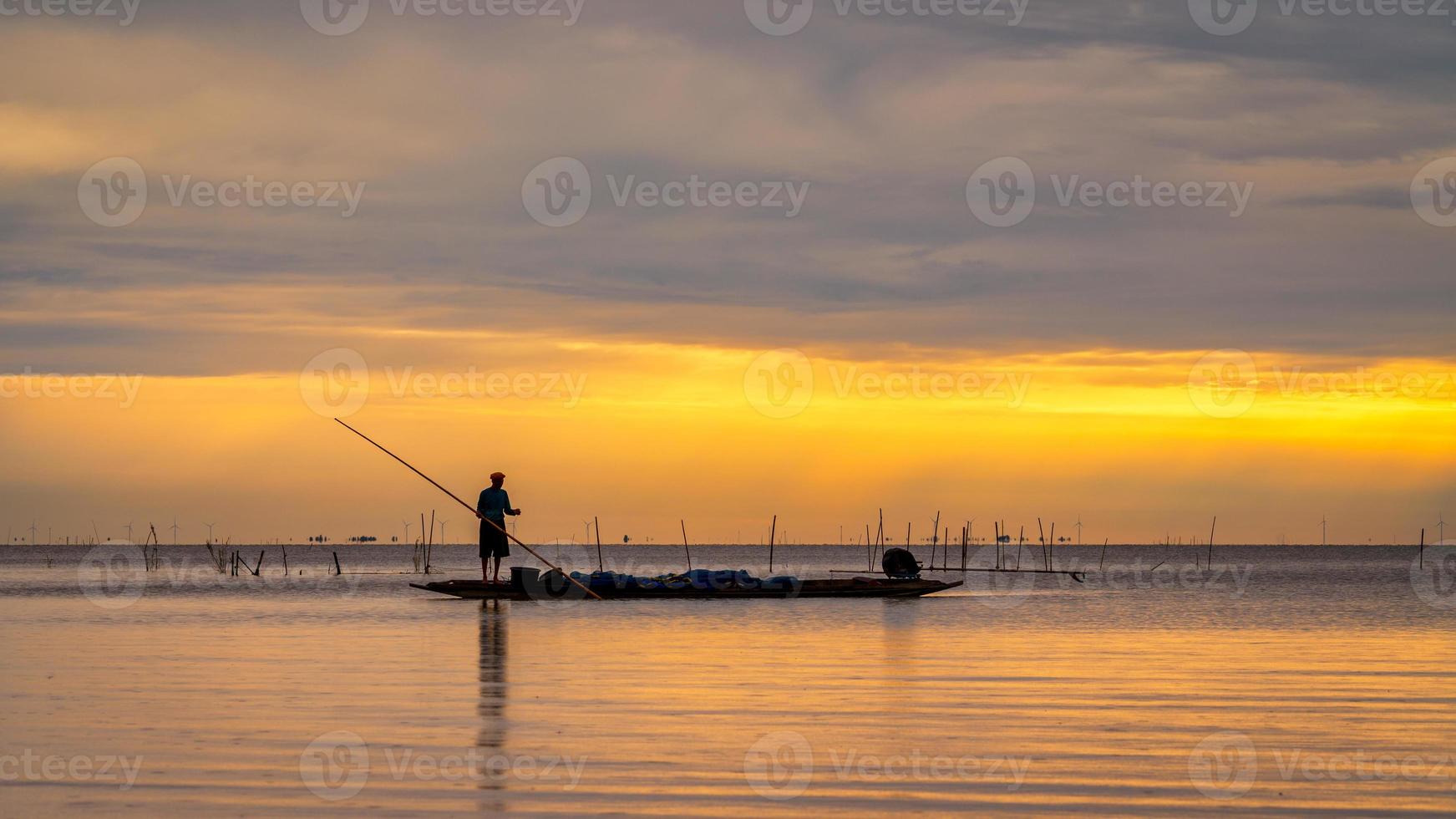 pescador asiático em barco de madeira para pescar no lago de manhã foto