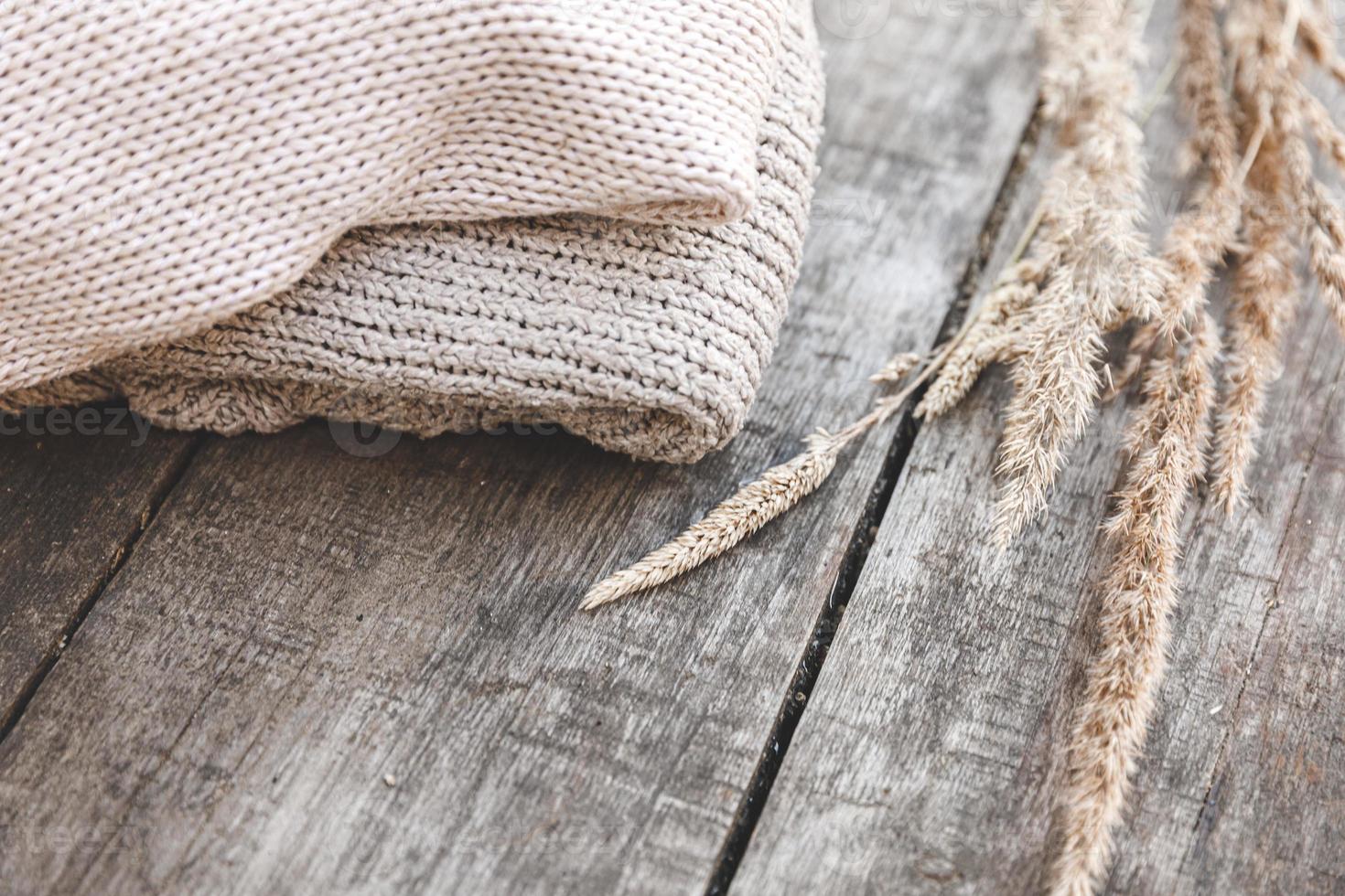 fundo de outono ou inverno. pilha de suéteres de roupas de lã de malha aconchegantes e plantas secas na mesa de madeira. humor hygge, conceito de clima frio. camisolas de malha feitas à mão. foto