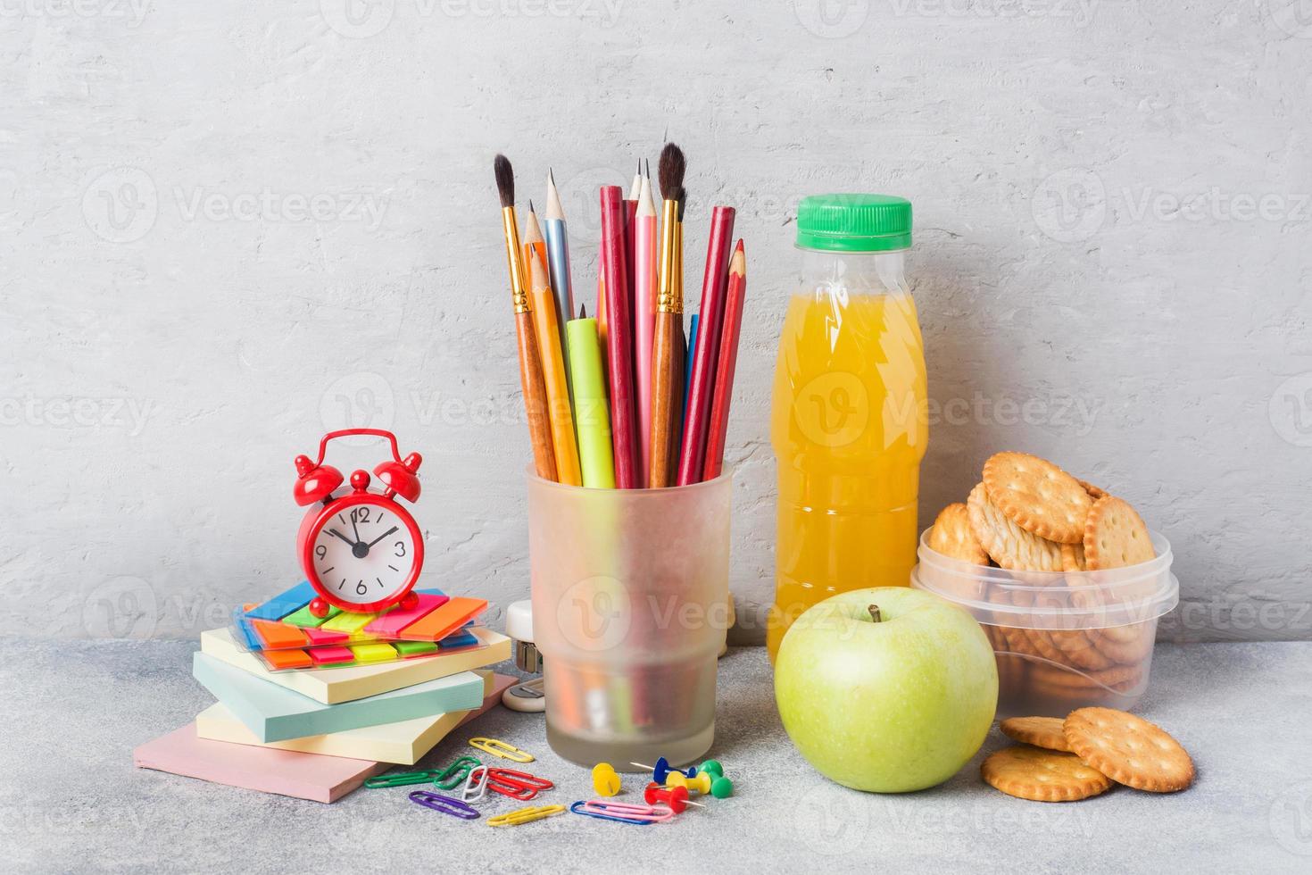 material escolar e biscoitos de café da manhã, suco de laranja e maçã fresca na mesa cinza com espaço de cópia. escola de conceito. foto