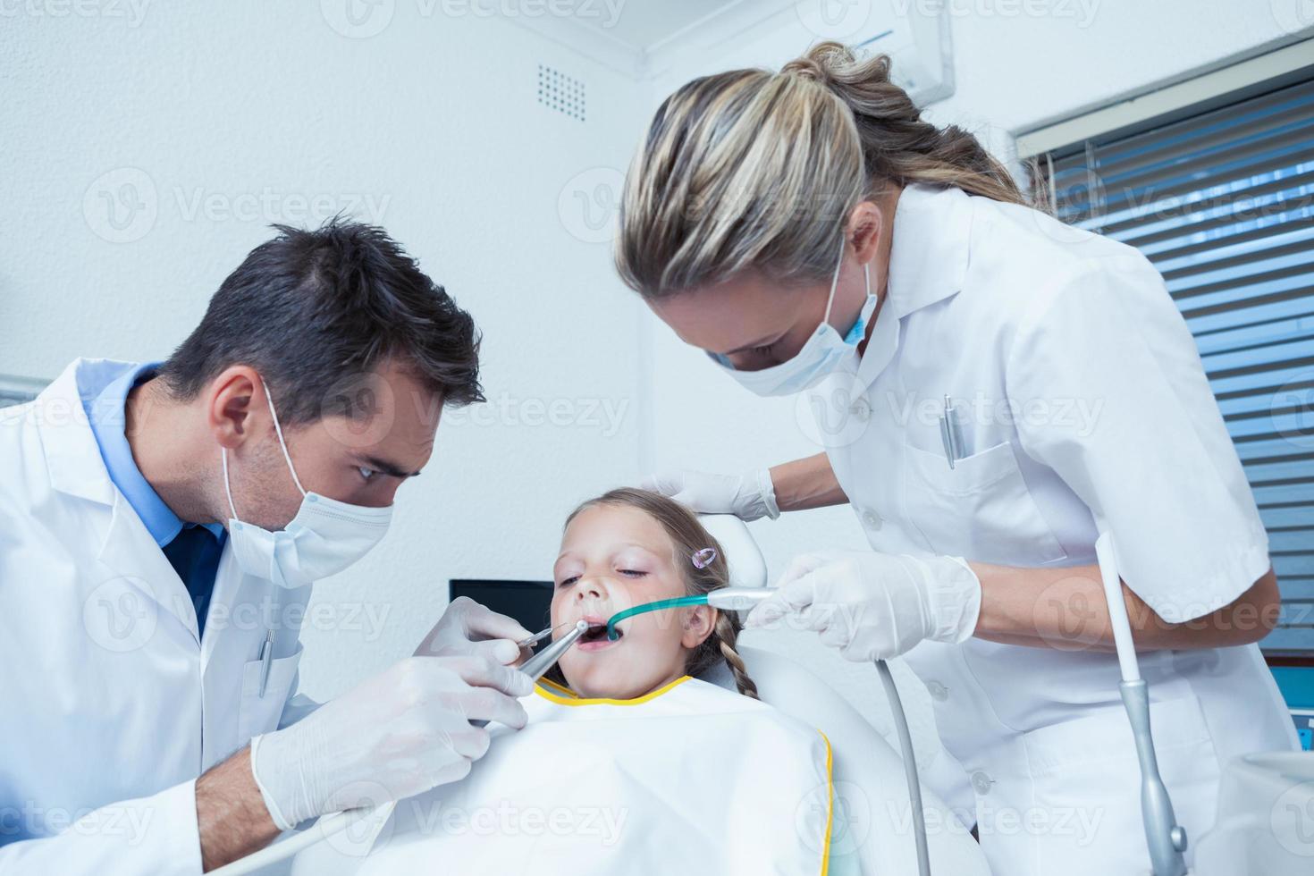 dentista masculina com assistente examinando os dentes das meninas foto