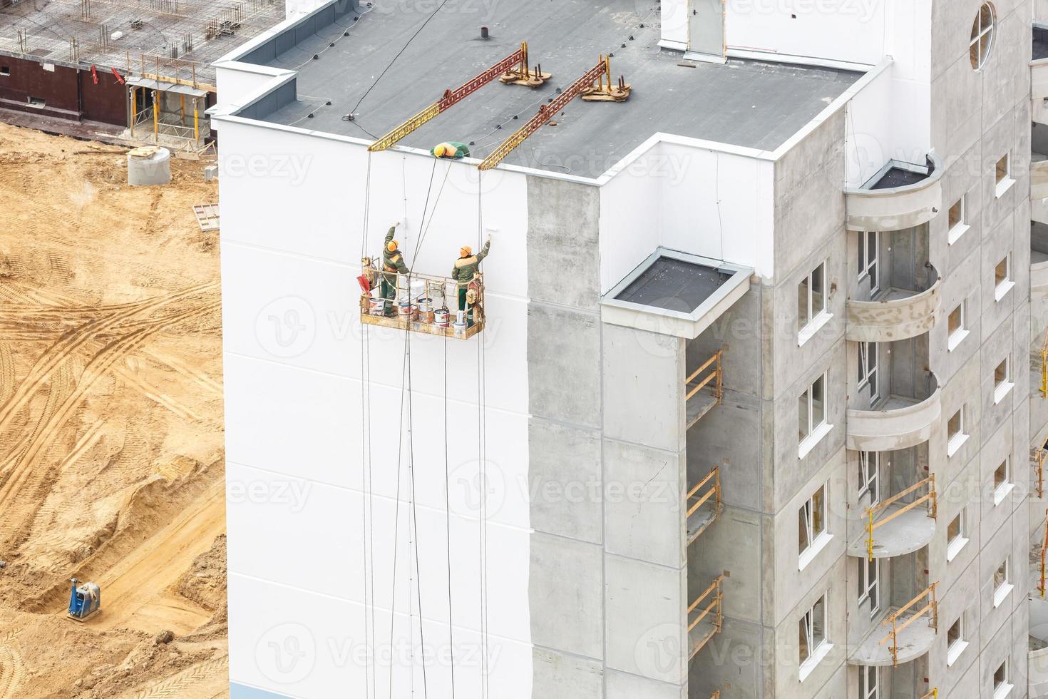 trabalhadores em um guindaste pintam a parede de um prédio residencial de uma vista aérea com floresta no fundo foto