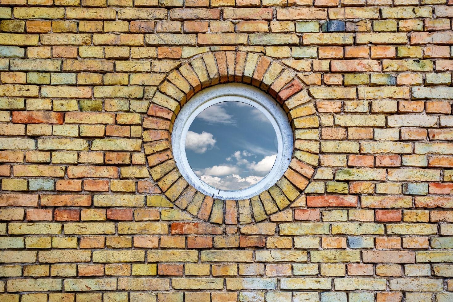 céu com nuvens refletidas em uma janela redonda na parede de tijolos foto