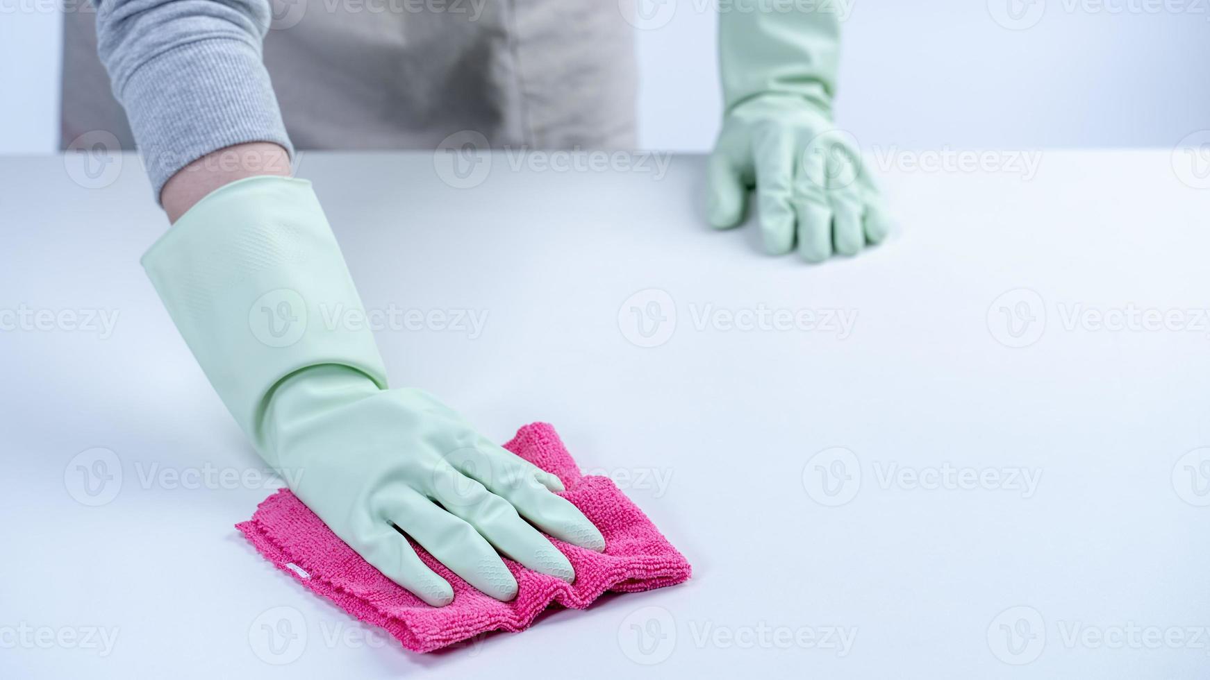 governanta de mulher usando luvas de proteção e usando um pano para limpar a superfície da mesa. foto