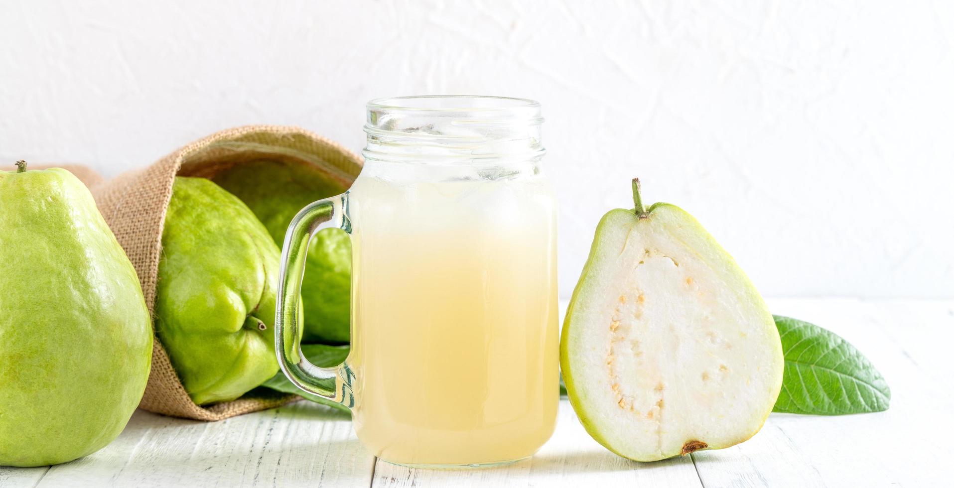 deliciosa goiaba com suco fresco em fundo de mesa de madeira branca. foto