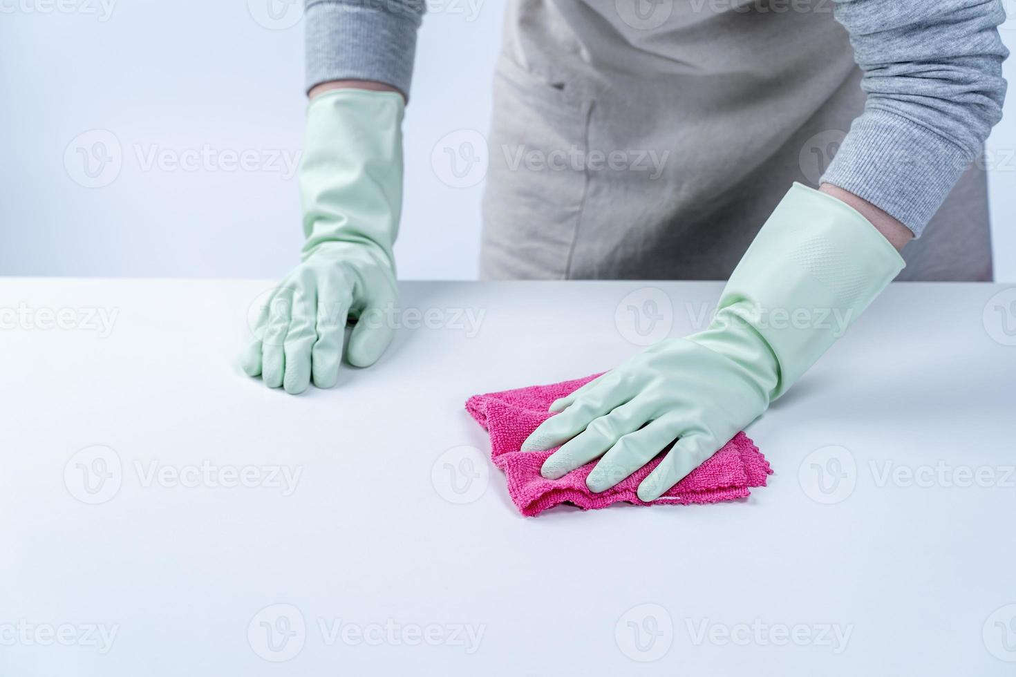 governanta de mulher usando luvas de proteção e usando um pano para limpar a superfície da mesa. foto