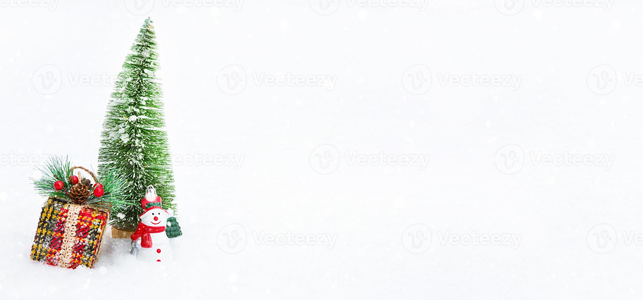 uma árvore de natal, uma caixa de presente e um boneco de neve de brinquedo na neve natural branca em uma queda de neve. decoração para o ano novo e natal, cartão com copyspace foto