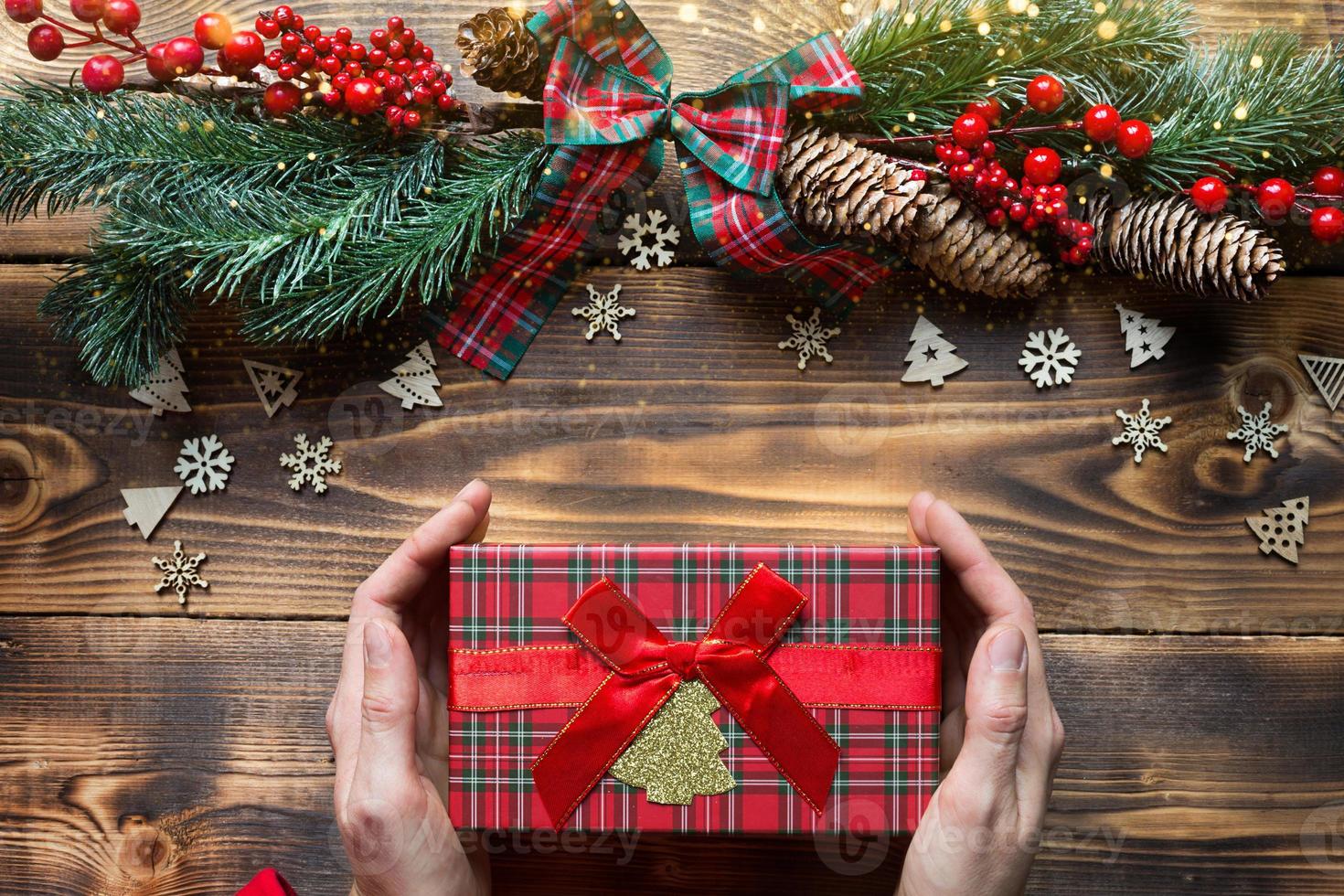 mãos segurando uma caixa de presente em um fundo de madeira de natal. ano novo, clima de férias, árvore de natal, flocos de neve, cones. copyspace, eco amigável, configuração plana. embalagem de férias foto