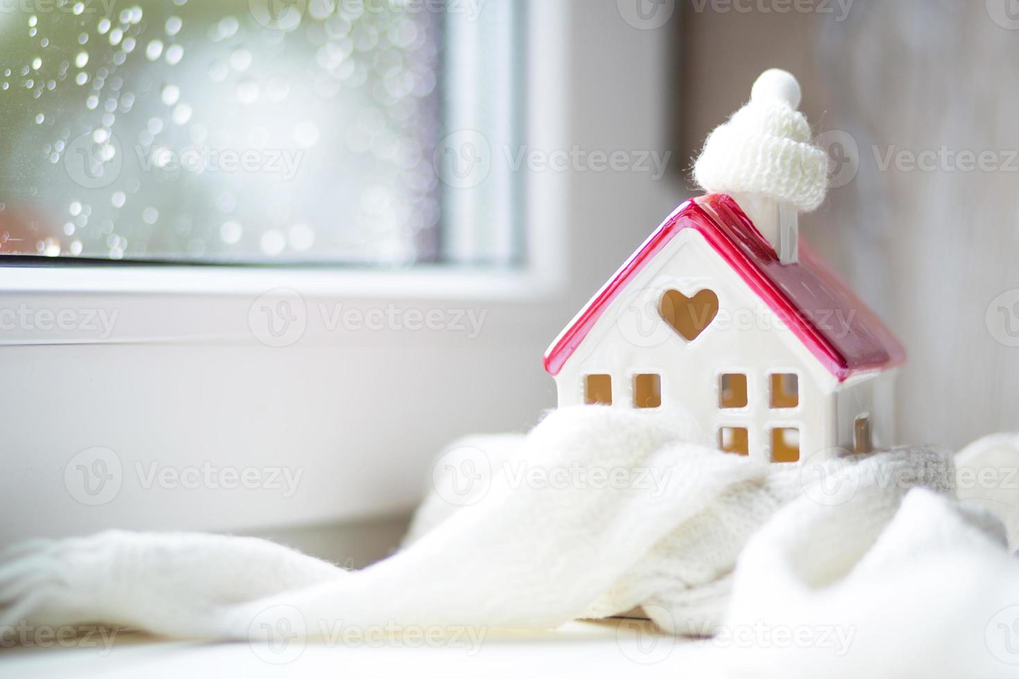 casa aconchegante está embrulhada em um chapéu e cachecol em uma decoração de peitoril da janela de tempestade de neve. inverno, neve - isolamento doméstico, proteção contra o frio e o mau tempo, sistema de aquecimento do ambiente. clima festivo, natal, ano novo foto