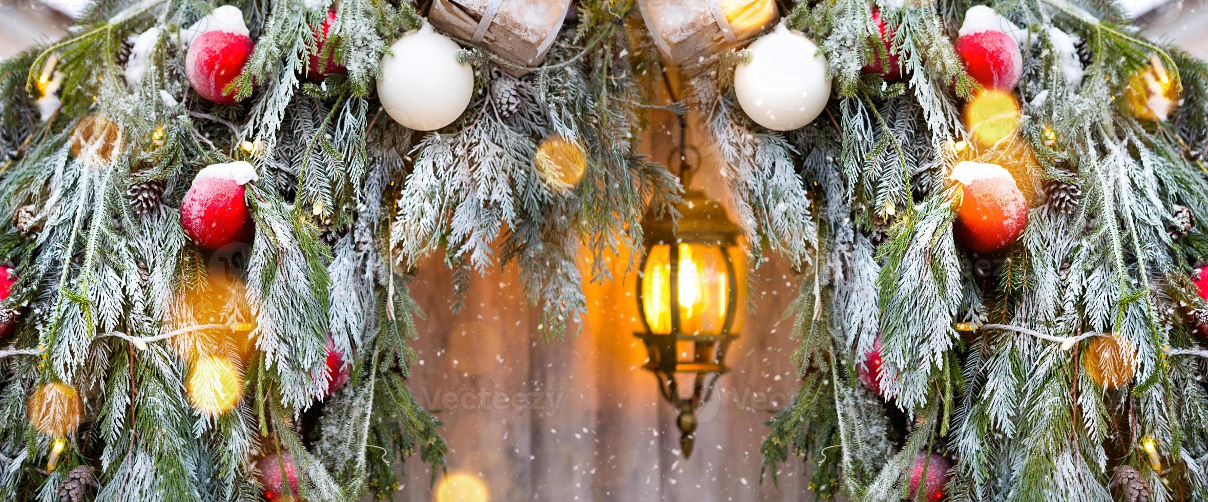 decorações de natal ao ar livre feitas de galhos de abeto natural, brinquedos, guirlandas e uma lanterna brilhante na neve em uma nevasca. inverno lá fora, queda de neve. decoração de ano novo foto