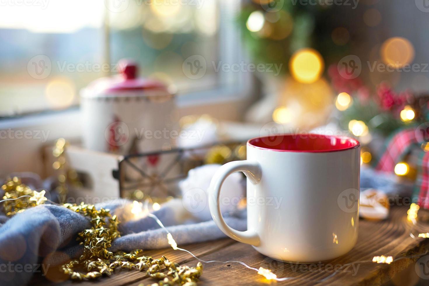 decoração de natal perto da janela em um aconchegante parapeito de madeira com uma caneca com uma bebida e um pote de biscoitos. luzes de fadas, galho de árvore de natal, bandeja de café da manhã ainda vida foto