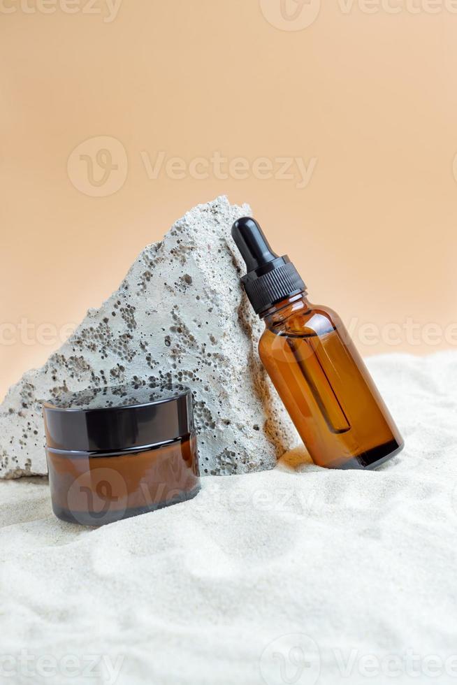 frascos de vidro âmbar escuro com soro com ácido hialurônico e creme facial na areia. cosmético orgânico spa natural. layout da marca do salão de beleza. brincar foto