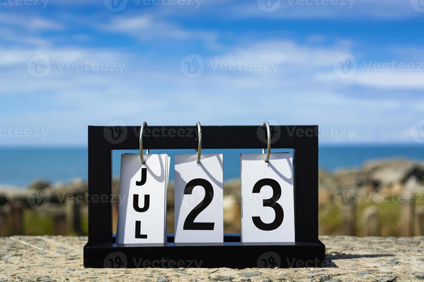 texto de data de calendário de 23 de julho na moldura de madeira com fundo desfocado do oceano. foto