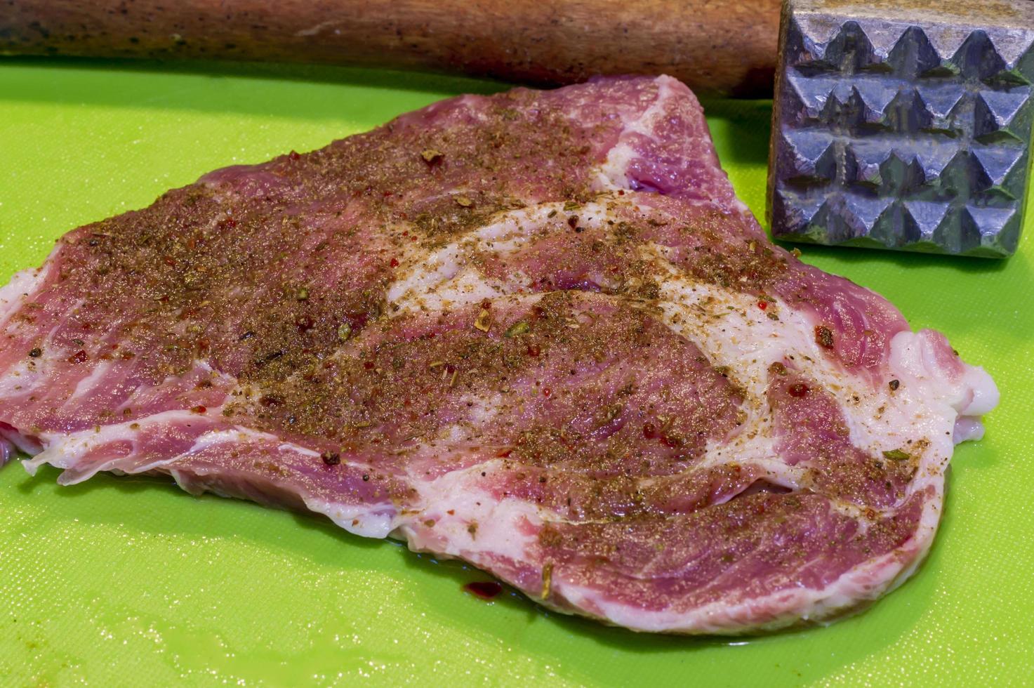 bife de porco cru com especiarias e amaciante de carne em fundo verde foto