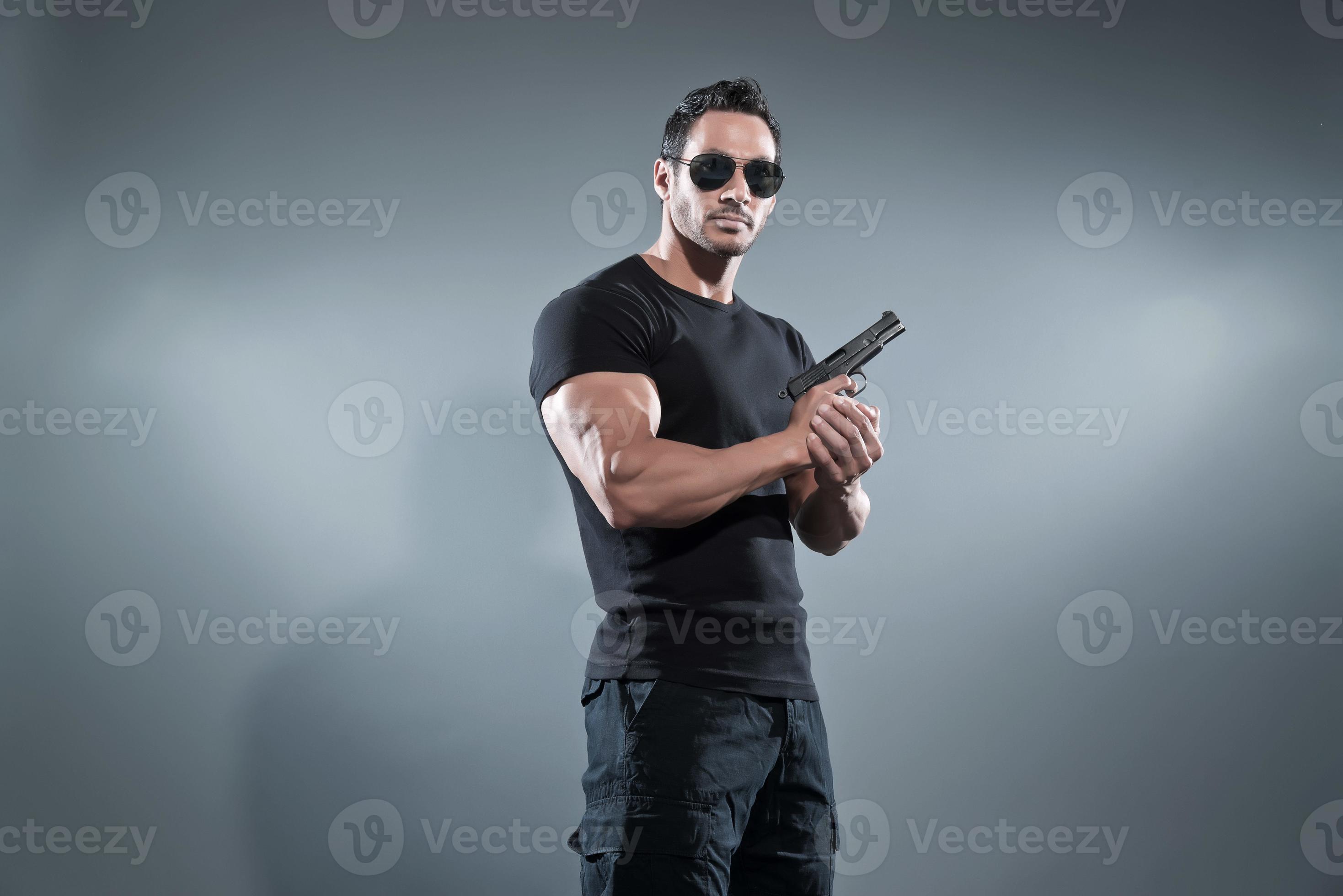 herói de ação musculoso homem segurando uma arma. vestindo camiseta preta. foto