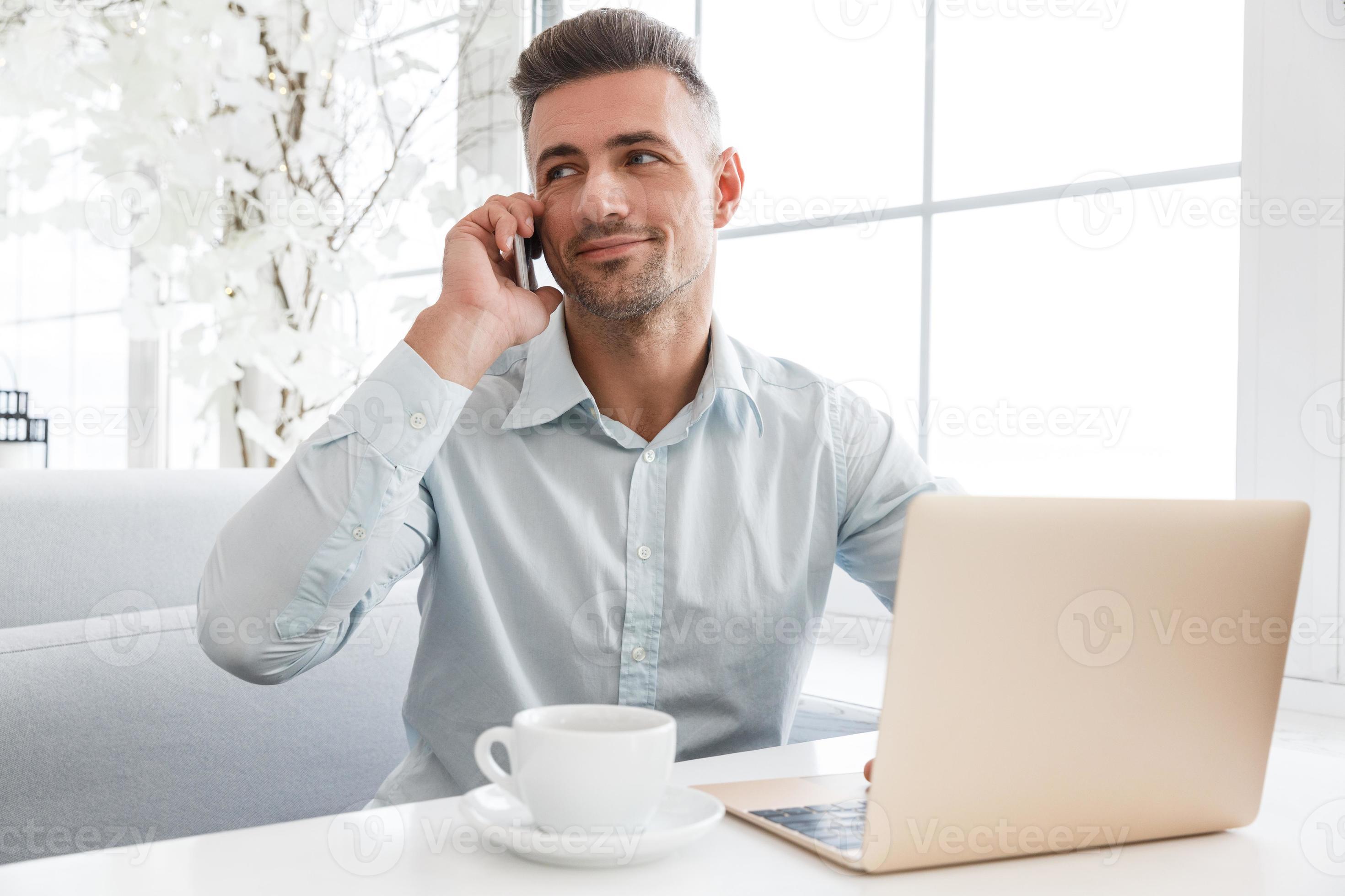empresário bonitão trabalhando com laptop e falando por telefone no café foto