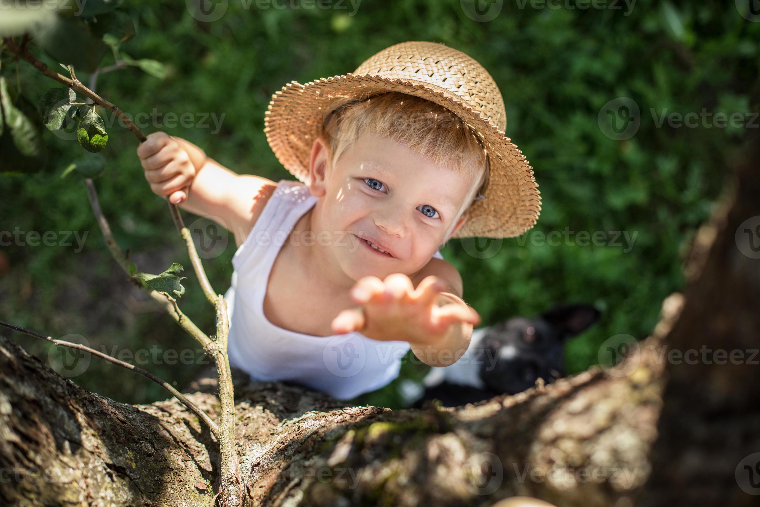 criança com chapéu de palha sobe em uma árvore foto